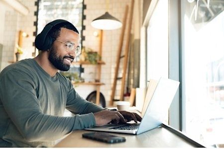 Man med hörlurar arbetar vid laptop nära ett ljust fönster